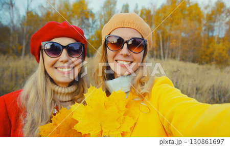 Happy young two women friends taking selfie with phone, autumn yellow leaves, girlfriends in park 130861697