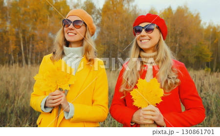 Happy young two women friends with autumn yellow leaves, stylish girlfriends smiles together in park 130861701
