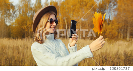 Happy smiling young woman taking pictures of yellow leaves on phone in autumn park 130861727