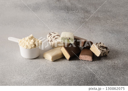 Protein bars with various coatings and sprinkles scoop of protein powder on gray background. Fitness nutrition. Close up. Protein bars with various coatings and sprinkles scoop of protein powder on gray background. Fitness nutrition. Close up. 130862075