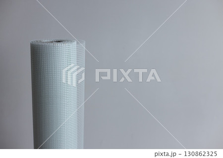 A roll of white plaster mesh for preparatory and painting works on a grey background . 130862325