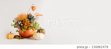Creative autumn floral arrangement of seasonal flowers in pumpkin as vase on gray background for Thanksgiving Day. Annual decorations. Copy space. Banner. Creative autumn floral arrangement of seasonal flowers in pumpkin as vase on gray background for Thanksgiving Day. Annual decorations. Copy space. Banner. 130862479