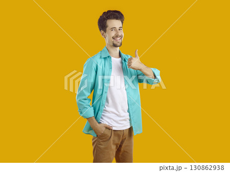 Happy, handsome groomed young man with neatly shaved beard and mustache smiles and gives thumbs up on isolated yellow background. Happy, handsome groomed young man with neatly shaved beard and mustache smiles and gives thumbs up on isolated yellow background. 130862938