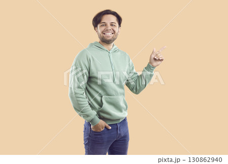 Smiling happy bearded guy is pointing index finger on copy space on beige background. Smiling happy bearded guy is pointing index finger on copy space on beige background. 130862940