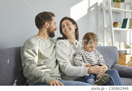 Happy parents and their toddler baby sitting on sofa together 130862946