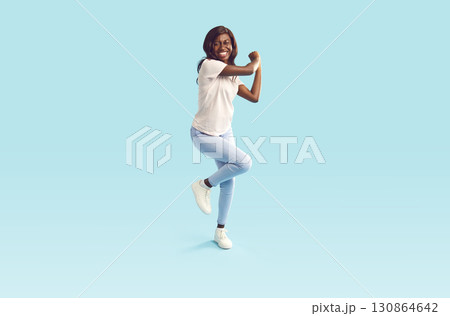 Happy young African American female dancer dancing on a light blue studio background 130864642