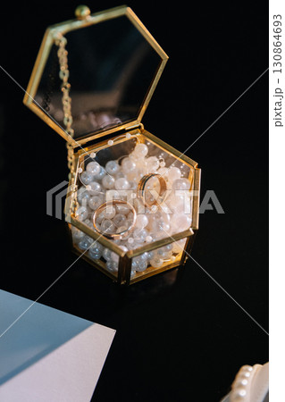 Two gold wedding rings in a glass box filled with decorative pearls on black background 130864693