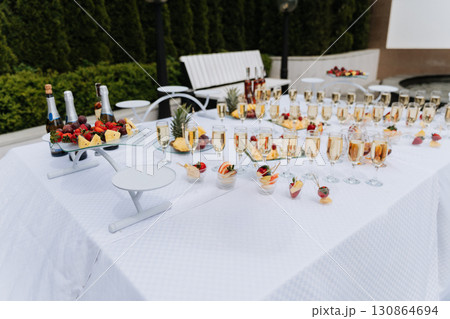 Outdoor buffet table with champagne, fruits and snacks arranged for a festive celebration Outdoor buffet table with champagne, fruits and snacks arranged for a festive celebration 130864694