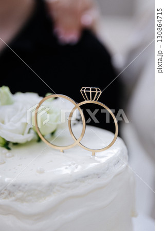 Wedding cake with floral decor and golden rings topper close up 130864715