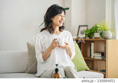 自宅のソファーでのんびりコーヒーを飲む50代のミドル女性 自宅のソファーでのんびりコーヒーを飲む50代のミドル女性 130864851
