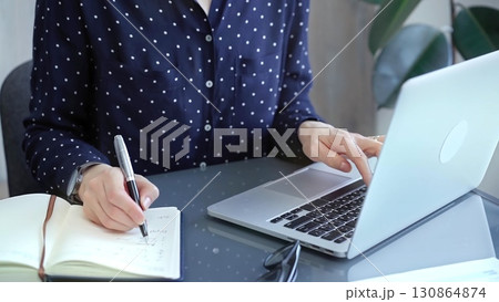Businesswoman professional writing in a notebook beside a laptop at a modern workplace, close up view. Business concept 130864874