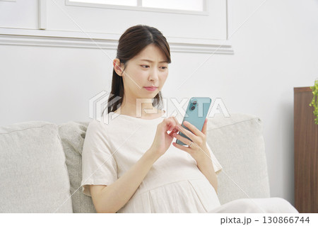 不安な表情でスマートフォンを使う妊婦　リビング 130866744