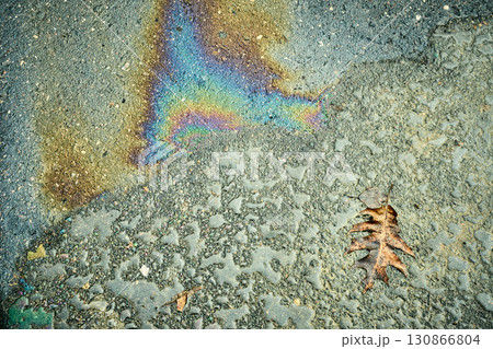 Oil spill creating a colorful rainbow sheen on a wet asphalt surface with a dry leaf Oil spill creating a colorful rainbow sheen on a wet asphalt surface with a dry leaf 130866804