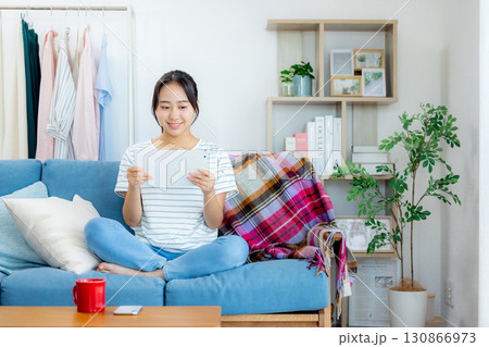リビングでコーヒーを飲みながらタブレットを見る若い女性 リビングでコーヒーを飲みながらタブレットを見る若い女性 130866973