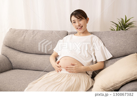 ソファーに座ってお腹をさする妊婦さん ソファーに座ってお腹をさする妊婦さん 130867382