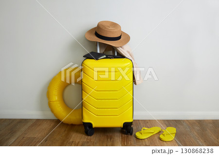 On yellow suitcase there is a straw hat and travel documents. On yellow suitcase there is a straw hat and travel documents. 130868238