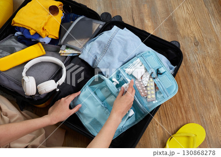 A woman puts hygiene products, clothes, a travel guide, headphones and travel accessories in a suitcase 130868278