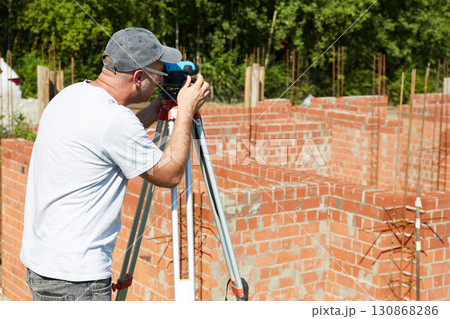 A construction worker checks the height level of the brickwork using a measuring tool on the construction site. A construction worker checks the height level of the brickwork using a measuring tool on the construction site. 130868286