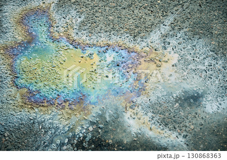 An oil slick on wet pavement refracts light, creating a vibrant array of colors and patterns, showcasing nature's art in a bustling city environment after rainfall. 130868363