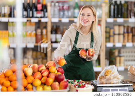 Young woman seller weighs apples in grocery store Young woman seller weighs apples in grocery store 130868586