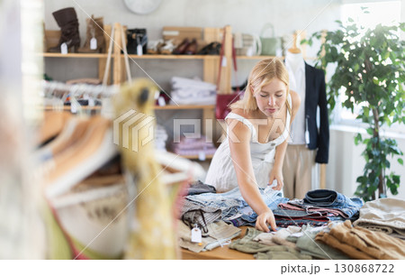 Young woman choosing pants on a shelf in a store Young woman choosing pants on a shelf in a store 130868722