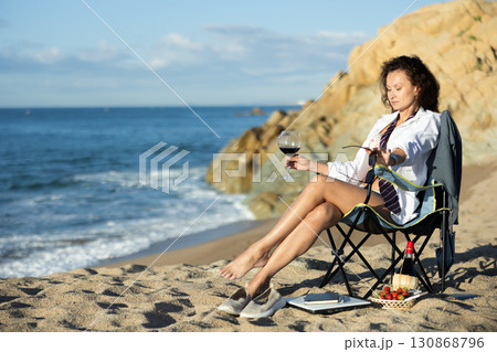 Seductive businesswoman with glass of wine near shoreline during picnic 130868796