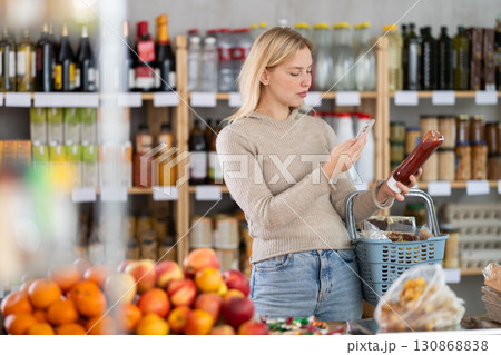 Female shopper scanning QR code on bottle ketchup label in grocery department of shop Female shopper scanning QR code on bottle ketchup label in grocery department of shop 130868838