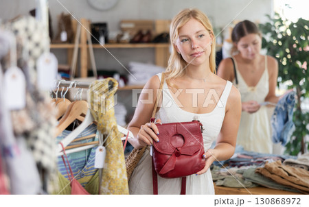 Young girl near showcase examine goods, buying handbag. Client looking for something in background Young girl near showcase examine goods, buying handbag. Client looking for something in background 130868972