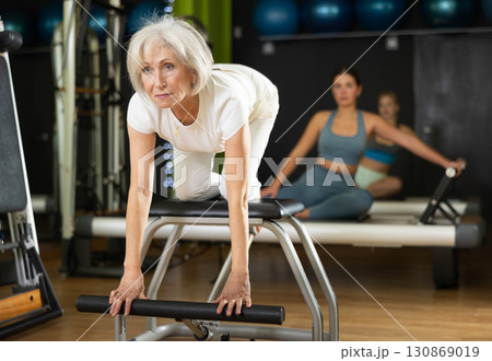 Senior woman perform pilates exercises using lifes beach pilates chair 130869019