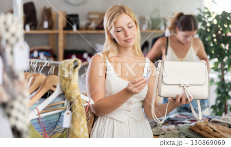 Young girl near showcase examine goods, buying handbag. Client looking for something in background Young girl near showcase examine goods, buying handbag. Client looking for something in background 130869069