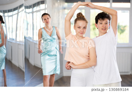 Experienced dance teacher teaching ballroom dancing to a couple of teenagers in studio Experienced dance teacher teaching ballroom dancing to a couple of teenagers in studio 130869184