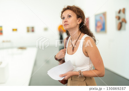 Interested woman examining paintings on walls in art gallery 130869287