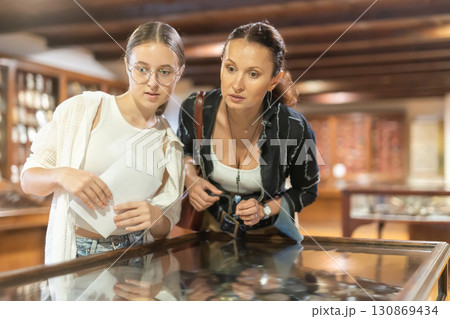 Young woman with teen daughter visitors stands near horizontal glass display case Young woman with teen daughter visitors stands near horizontal glass display case 130869434