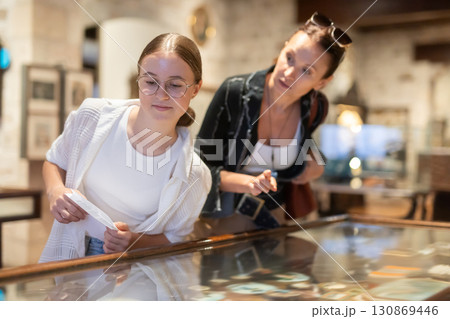 Young woman with teen daughter visitors stands near horizontal glass display case Young woman with teen daughter visitors stands near horizontal glass display case 130869446
