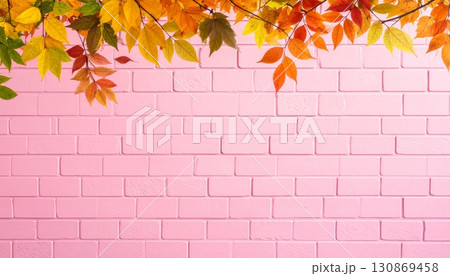 Autumn maple leaves in shades of red, orange, and yellow cling to a rustic pink brick wall, creating a vibrant seasonal frame 130869458