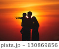 (AI生成)家族イメージ　寄り添う若い親子の夕陽のシルエット 130869856
