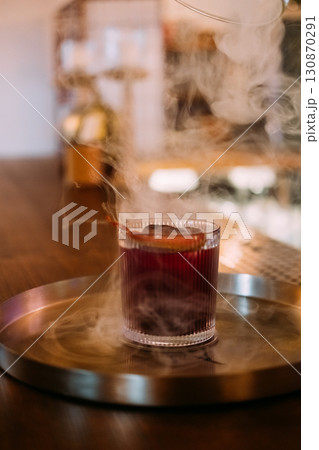 Negroni glass. Smoke drink. Red alcoholic cocktail served with ice cube citrus slice peel. Aromatic refreshing liquor mix on pub counter. Negroni glass. Smoke drink. Red alcoholic cocktail served with ice cube citrus slice peel. Aromatic refreshing liquor mix on pub counter. 130870291
