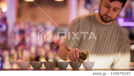 Barman pouring liquid. Asian pub. Bartender filling portioned small ceramic cups for sake. Man serving traditional japanese alcoholic order. 130870297