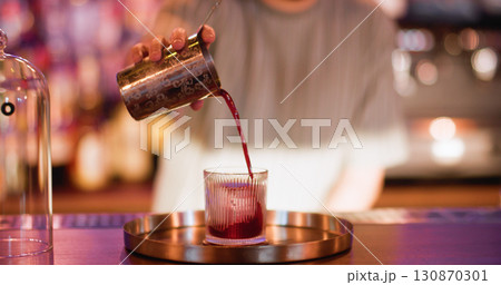 Serving drink. Preparing liquor. Bartender pouring red strained liquid from metal shaker. Professional making refreshing beverage. Serving drink. Preparing liquor. Bartender pouring red strained liquid from metal shaker. Professional making refreshing beverage. 130870301