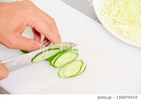 サラダ用にキュウリを薄切りする男性の手元のクローズアップ。食事の準備をする男性の連続写真。 130870410