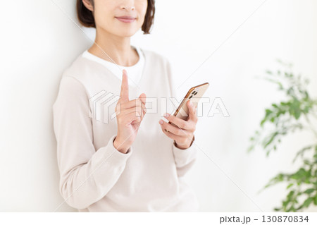 スマホを持って人差し指を立てるカジュアルのミドル女性ビジネスウーマン 130870834