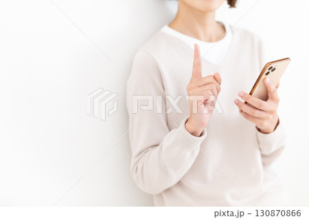 スマホを持って人差し指を立てるカジュアルのミドル女性ビジネスウーマン 130870866