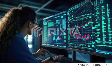 Woman analyzing financial data on multiple computer screens. 130871045