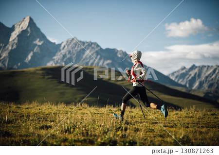 Fitness woman trail runner running in grassland with snow capped mountains in the background Fitness woman trail runner running in grassland with snow capped mountains in the background 130871263