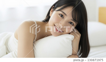 枕を抱きしめて幸せそうに微笑むキャミソール姿の女性 130871975