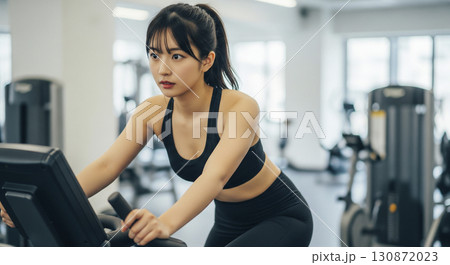 エアロバイクを漕ぐ若い女性 130872023