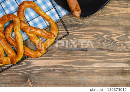 Top view of pretzel loaf and sausage with a blue checkered tablecloth or napkin on a wooden table background. Copy space. Concept of Oktoberfest. Bavarian German culture festival decoration symbol 130873012