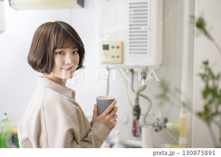 マグカップを持ってキッチンに立つ若い女性 130873891