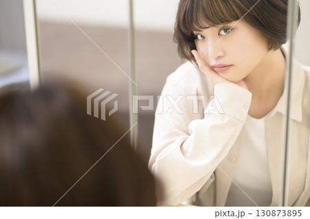 メイクをする女性の鏡越しのポートレート メイクをする女性の鏡越しのポートレート 130873895