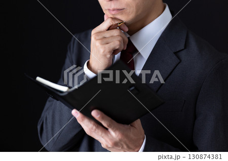 手帳を見て考え事をするスーツを着たミドル男性ビジネスマン 130874381